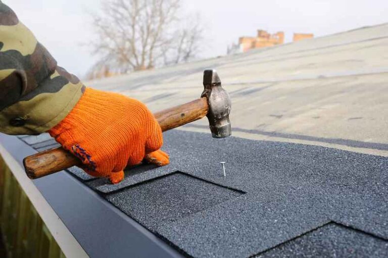 Hand hammering nail into roof shingles.